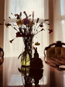 A room with curtains drawn and a table with a vse of flowers and an ornament